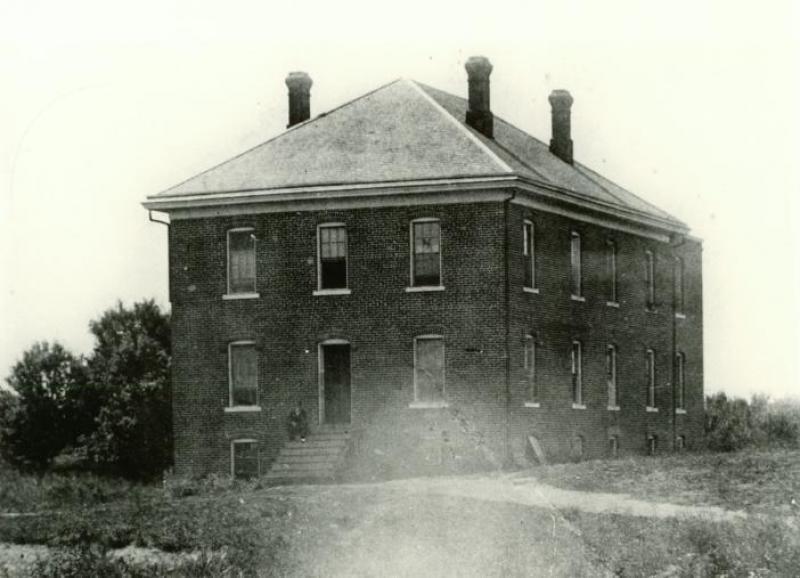 Back side of Boarding Cottage West with man sitting on the back stoop. 