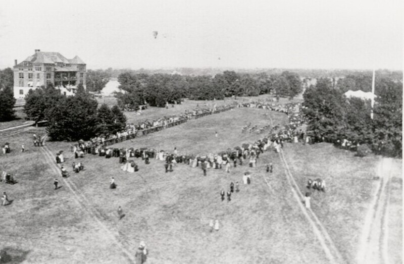 Crowds gathered in a circle on the lawn south of Botany Hall which stands in the distance.