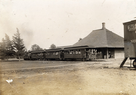 Photograph of the Dinkey stopped in front of the Hub. The engine pulls three passenger cars loaded with students either just arriving on campus or preparing to leave for downtown Ames.