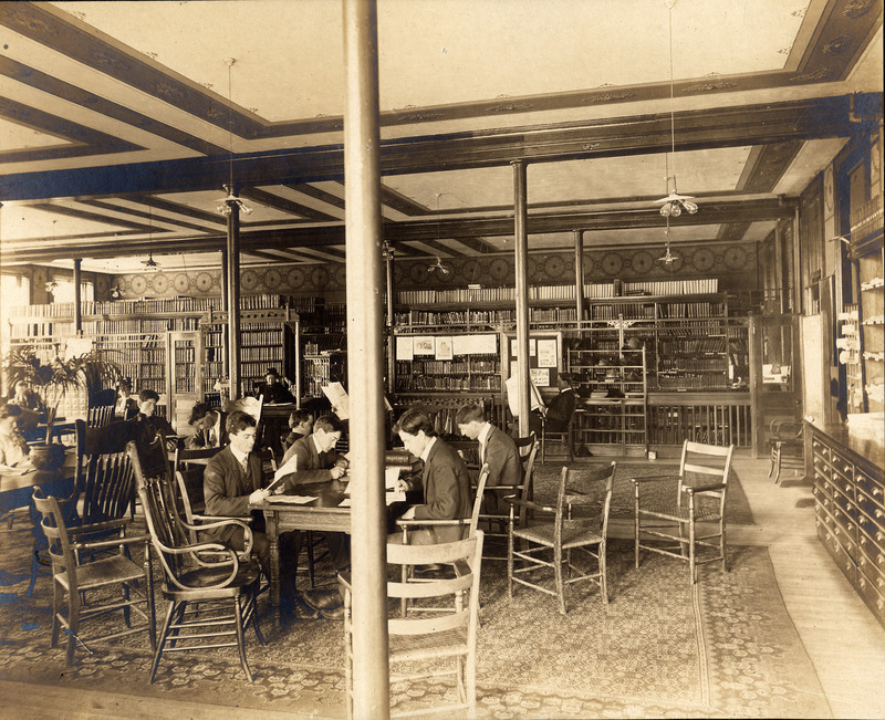 People sit at tables throughout the library reading newspapers and books.