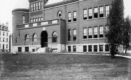 View of the front (east) side of Morrill Hall. A woman walking northwards is beside the main entryway to the building. Old Main is on the left side of the photo.